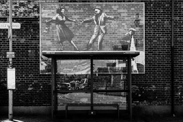 Admiralty Road, Great Yarmouth, Norfolk. Three people on top of a bus shelter: two dancing and another playing an accordion. The Banksy spraycation.