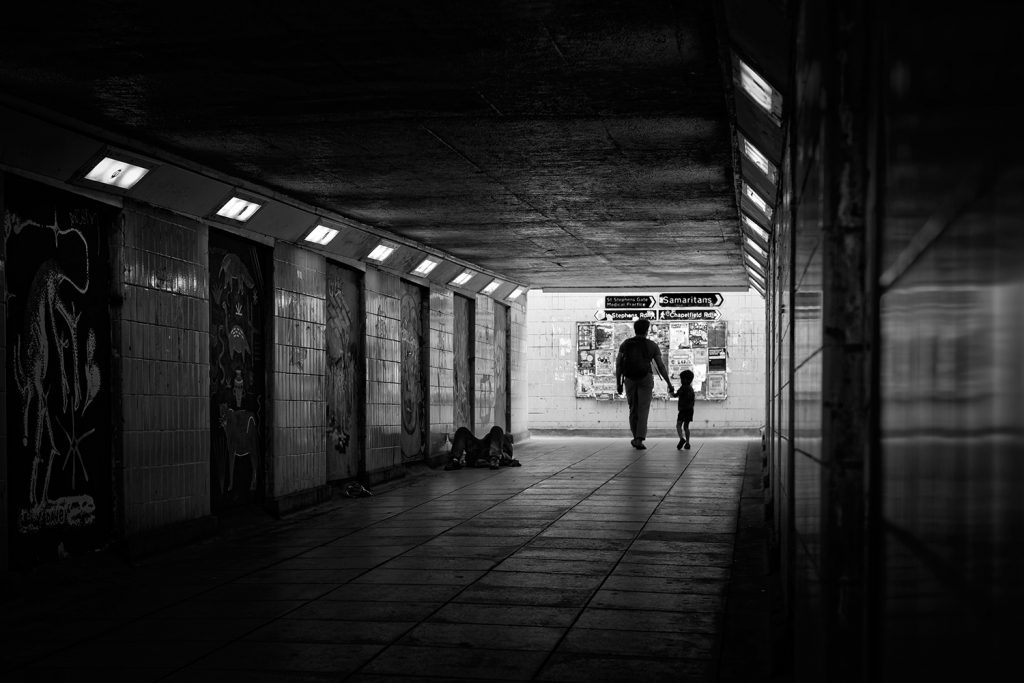A father and child pass a homeless person in an underpass in Norwich, Norfolk.